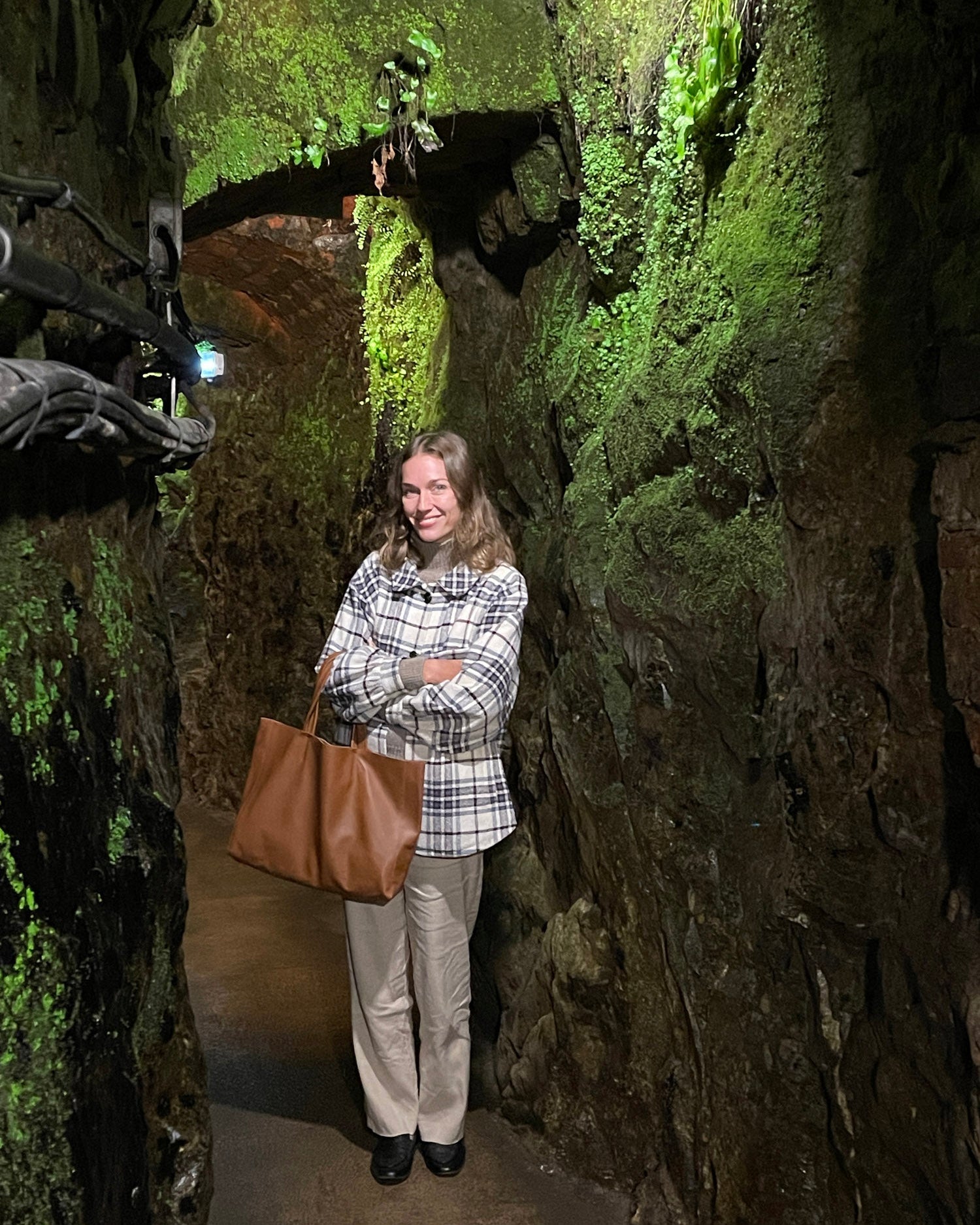 Woman standing in a narrow, moss-covered tunnel